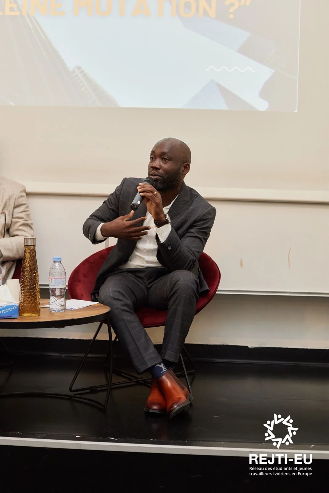 Un intervenant assis prend la parole au microphone lors d’une rencontre REJTI-EU